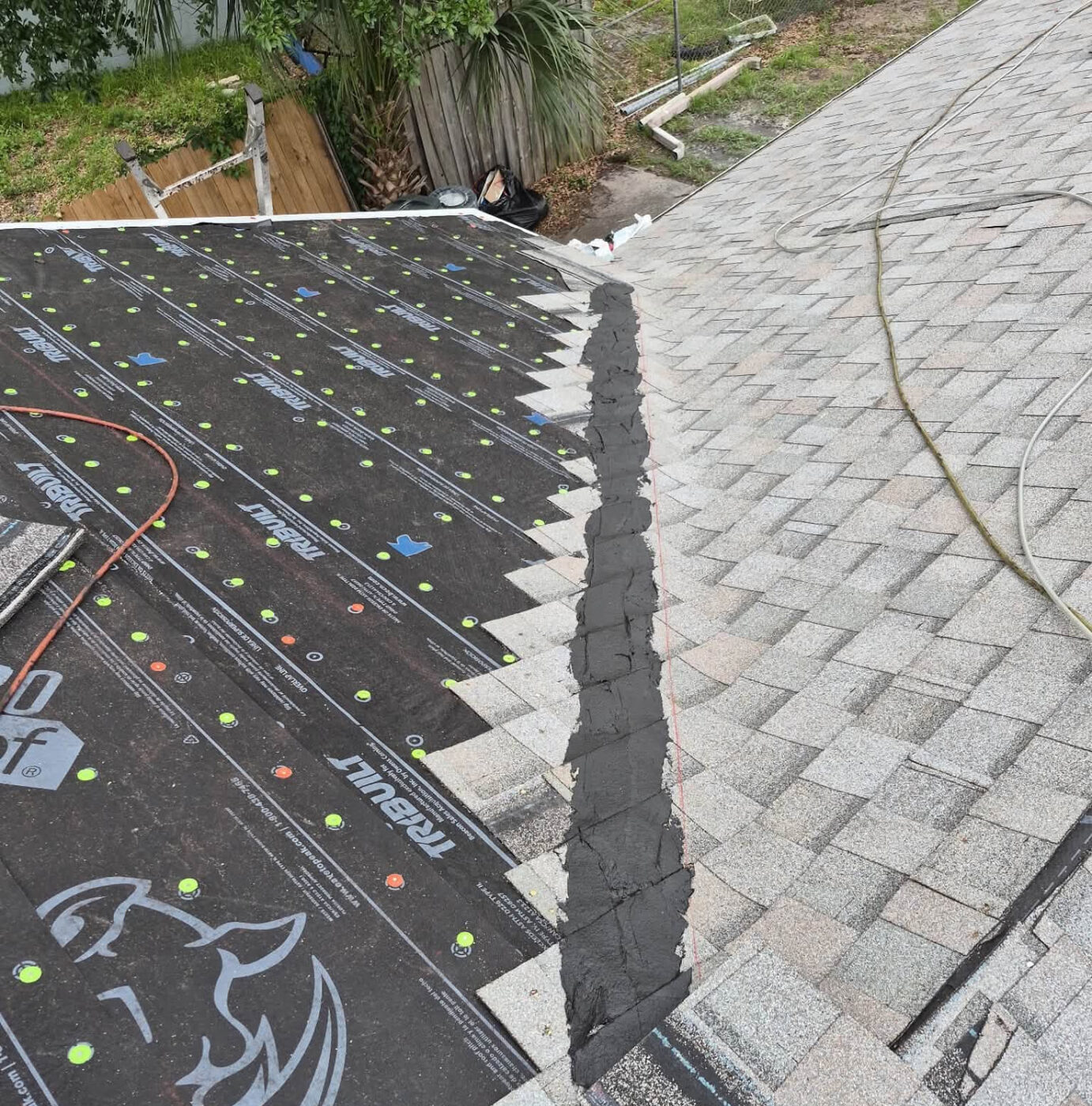 New synthetic underlayment going down beside existing shingles during a re-roof